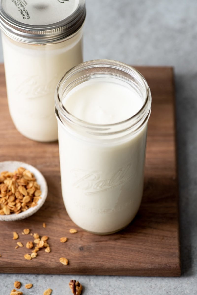 Tall glass jars filled with homemade yogurt, on a dark wooden cutting board