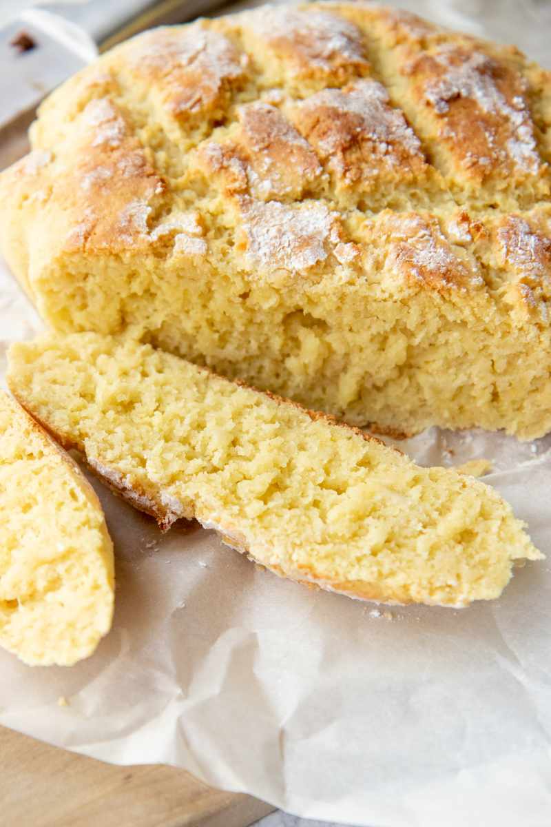 A loaf of crusty gluten-free bread sliced on crinkly parchment paper.