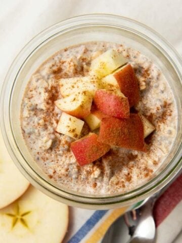 Top view of a glass jar of apple cinnamon overnight oats garnished with chopped apples and cinnamon.