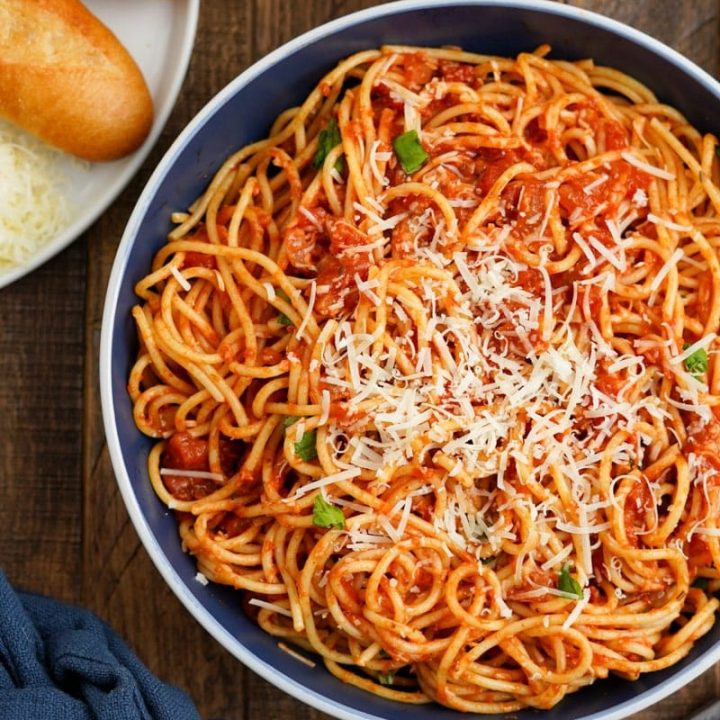 Top view of a pasta arrabbiata dinner served with bread, shredded parmesan cheese, and a side salad.