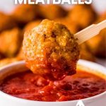 Close view of a baked chicken meatball being dipped into a bowl of marinara sauce on the end of a bamboo cocktail stick. A text overlay reads, "Baked Chicken Meatballs. Kids + Adults Love 'Em!"