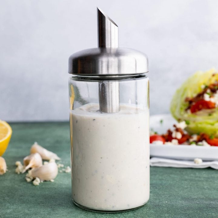 Homemade blue cheese dressing in a cruet in front of a wedge salad.