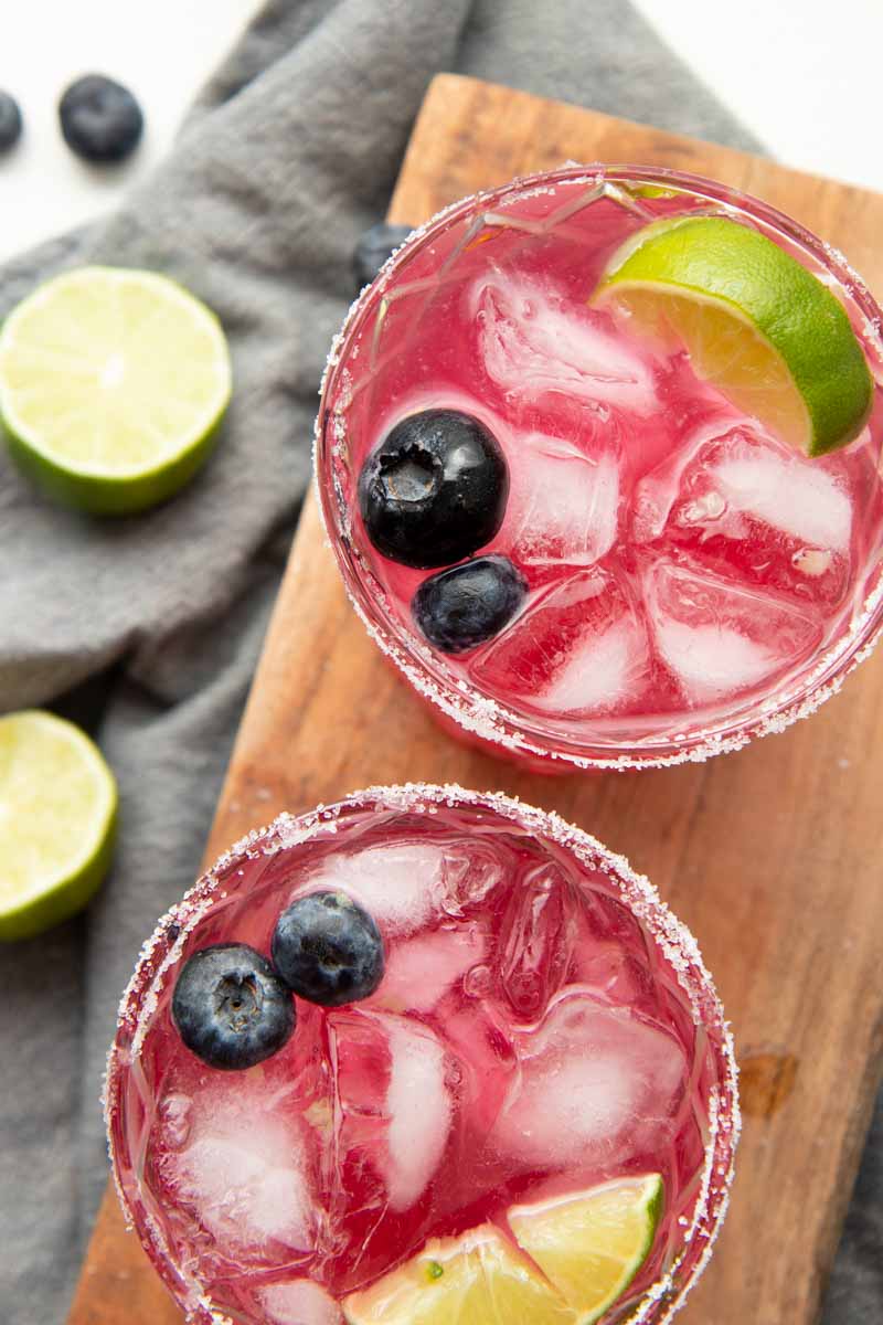 Top view of two blueberry margaritas with salt rims, fresh berries, and lime wedges garnishing the glasses.