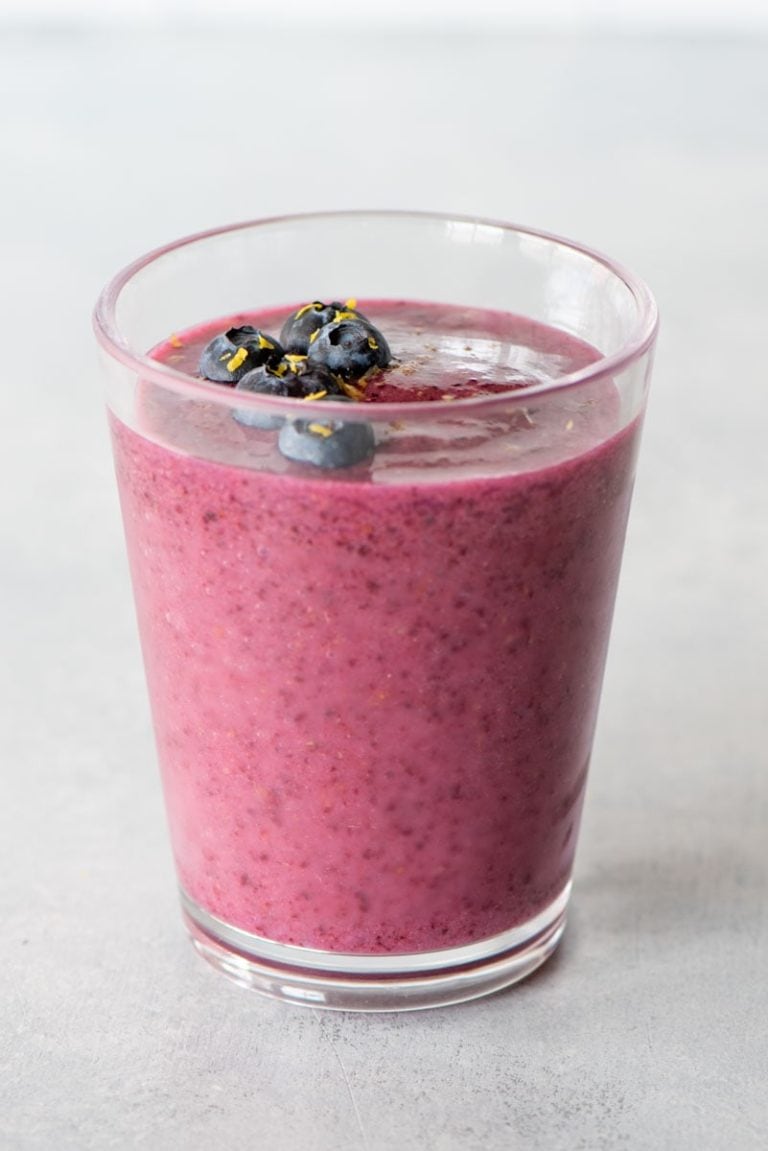 Top view of a blueberry smoothie topped with fresh berries and lemon zest.