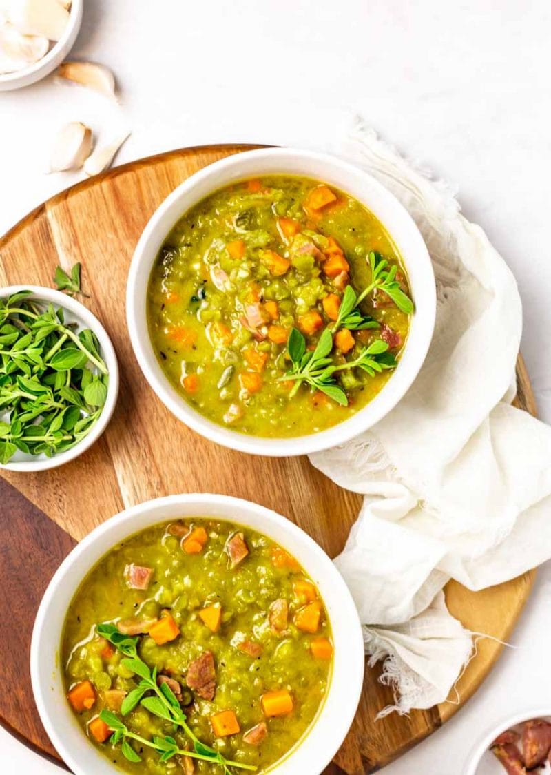 Overhead of two bowls of split pea and ham soup on a round wooden serving board.