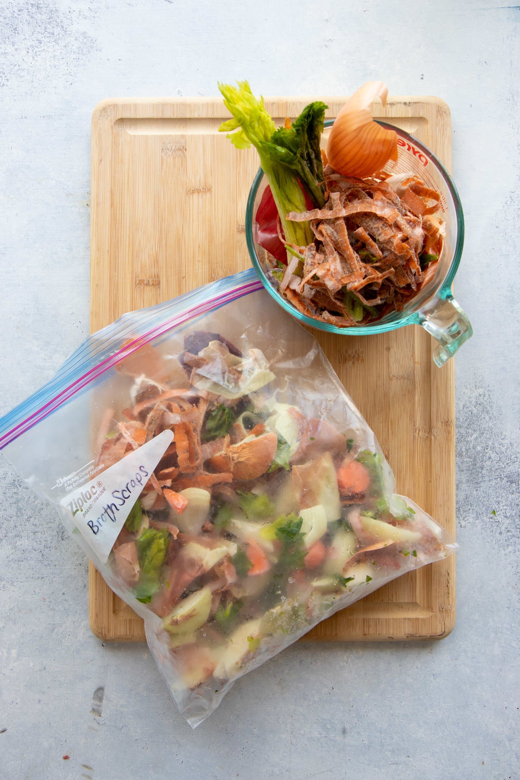 Overhead shot of veggie scraps in a glass measuring cup and in a freezer bag