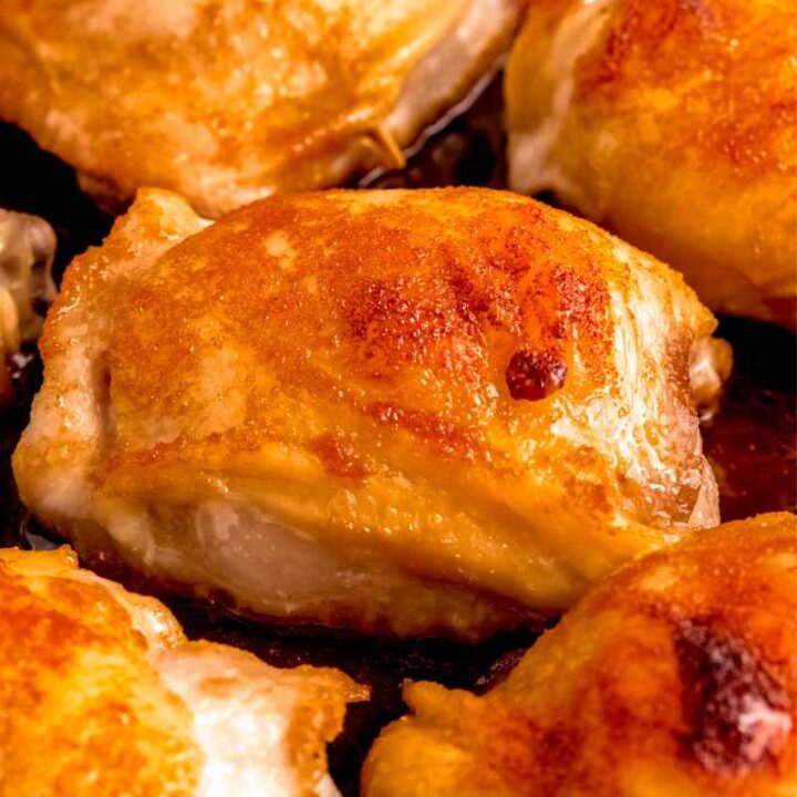 Tight view of a brown sugar chicken thigh in the center of a skillet with other thighs around it, all perfectly cooked and ready to serve.