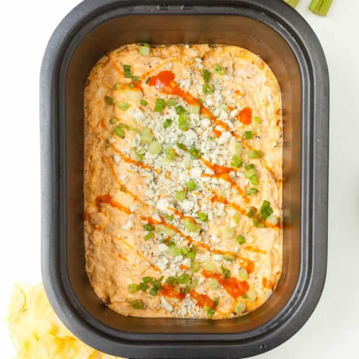 Overhead of a crockpot filled with finished dip, topped with garnishes with sticks of celery and an open bag of Kettle brand chips around.