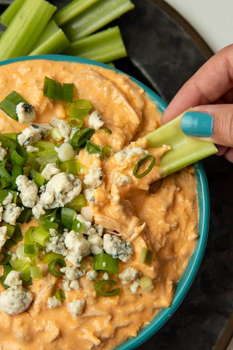 A hand scoops up buffalo chicken dip with a stick of celery.