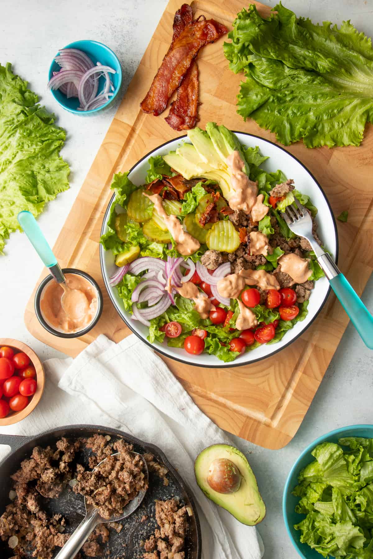 A burger bowl salad in a large white bowl sits on top of a cutting board, with a small dish of "special sauce" nearby.