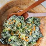 A large wooden bowl with kale caesar salad and crunchy chickpeas tossed in a homemade caesar dressing. A text overlay reads, "Superfood Caesar Salad."