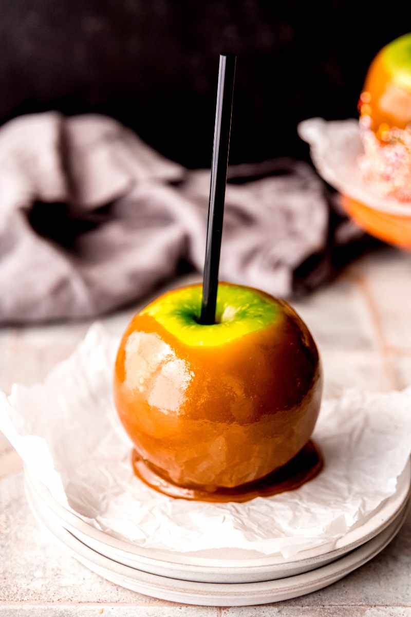 A caramel apple is served on a parchment paper lined plate.