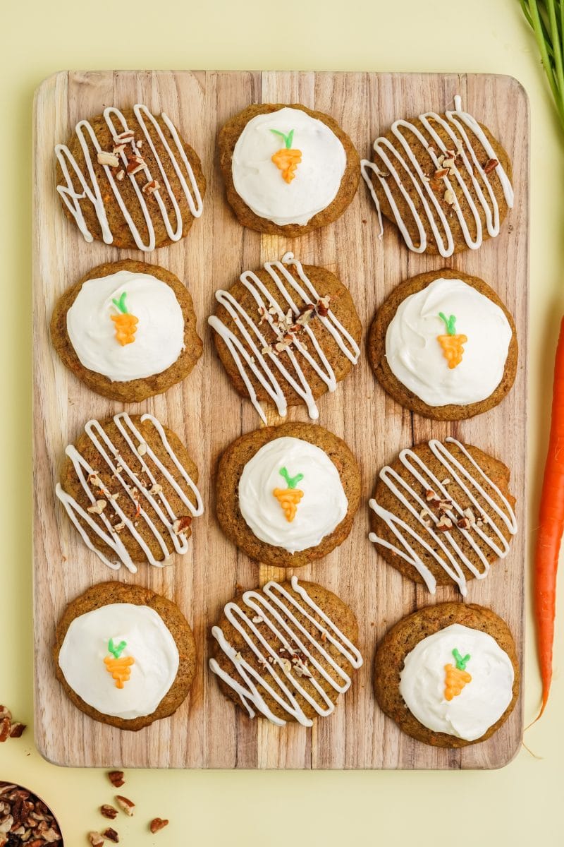 Birdseye view of frosted carrot cake cookies on a wooden cutting board.