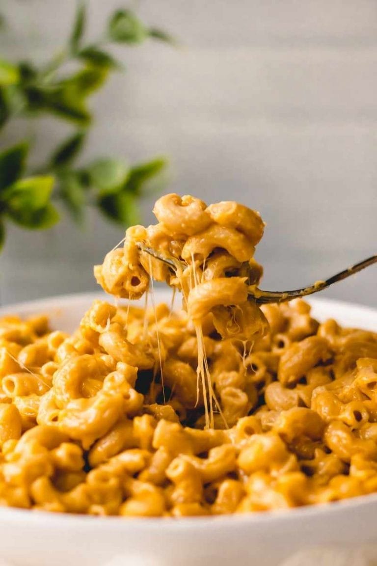 Close view of cheesy strands as a fork scoops up a bite of instant pot mac and cheese from a white bowl.