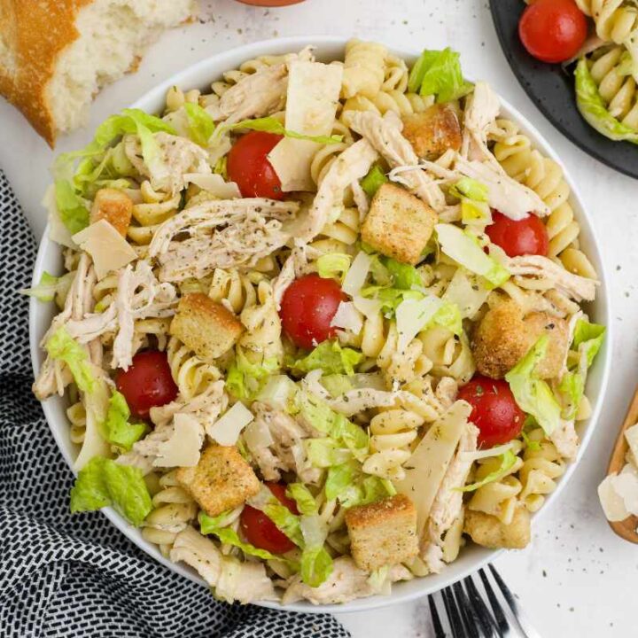 Top view of chicken caesar pasta salad dinner with bread, forks, and shaves parmesan around it.