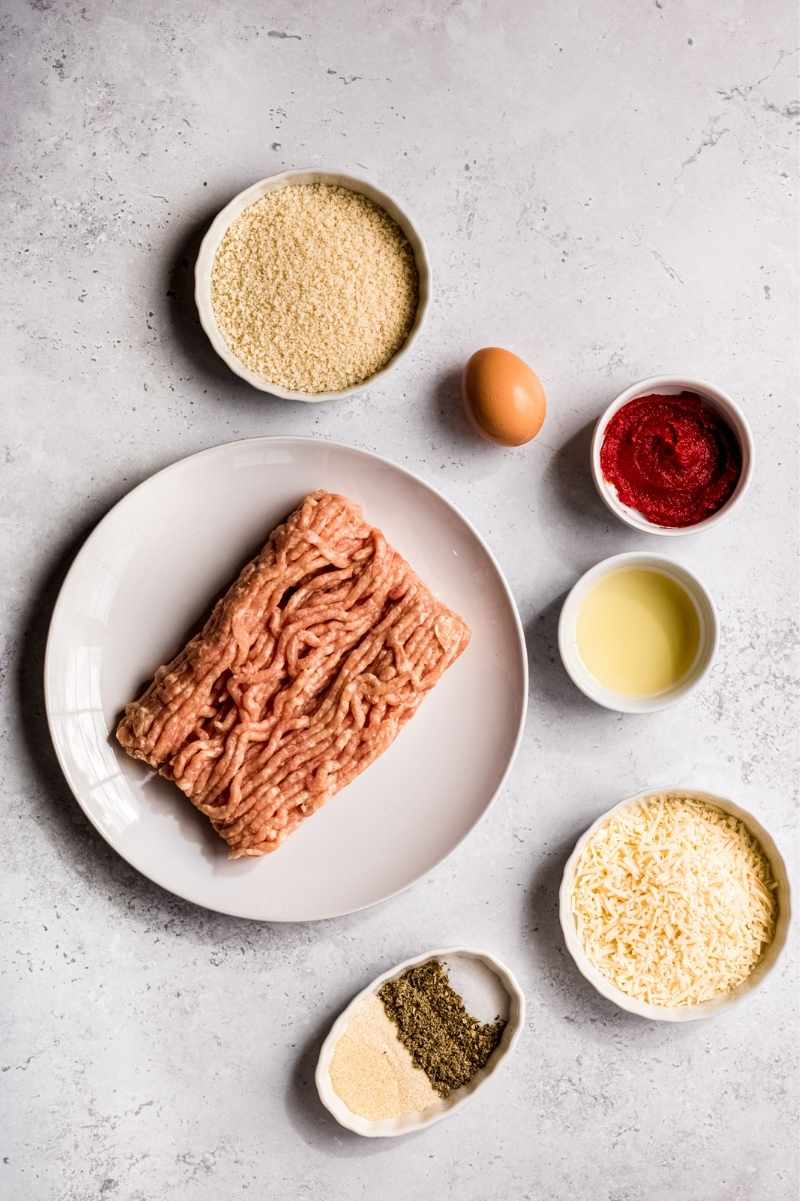 Overhead view of all the ingredients needed to make baked chicken meatballs, including ground chicken, breadcrumbs, and seasonings.