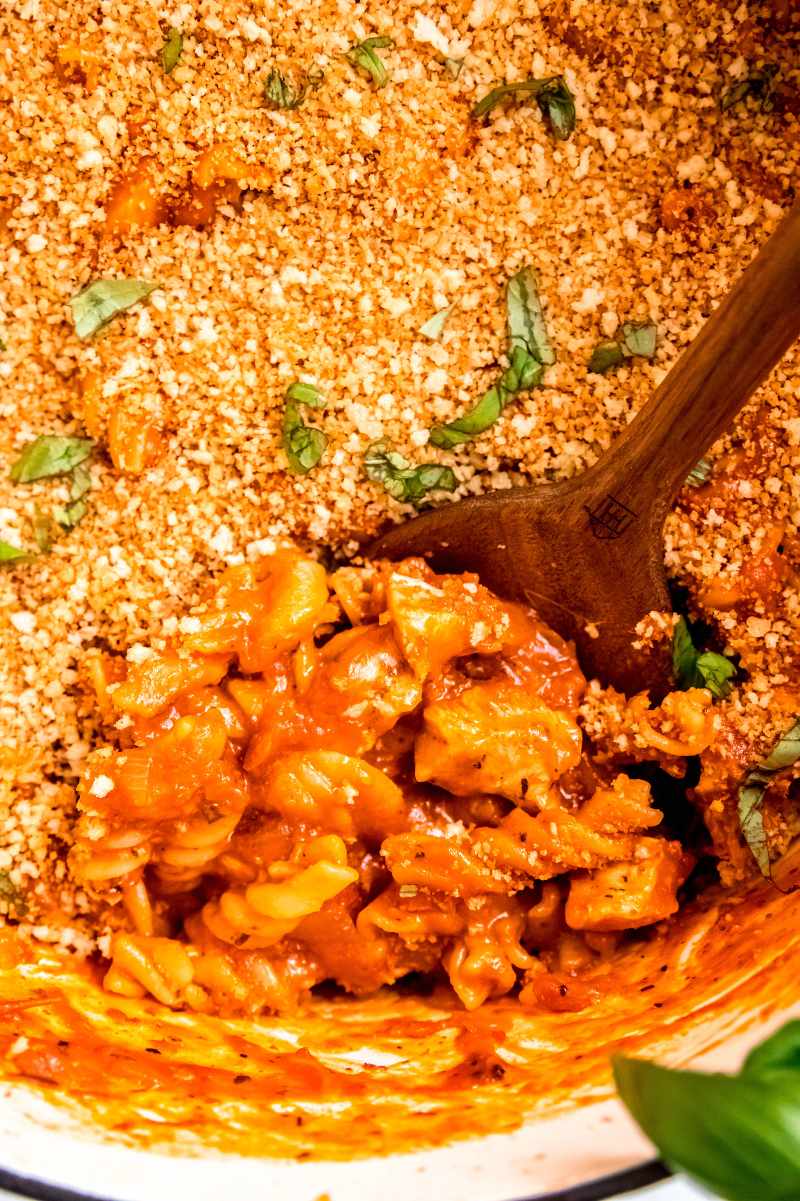 Close view of a wooden spoon scooping into a pot of chicken parmesan pasta.