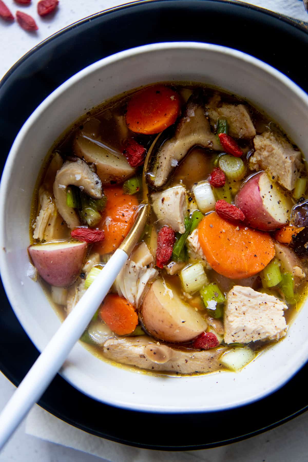 A spoon with a white handle sits in a white bowl full of Instant Pot herbal chicken soup.