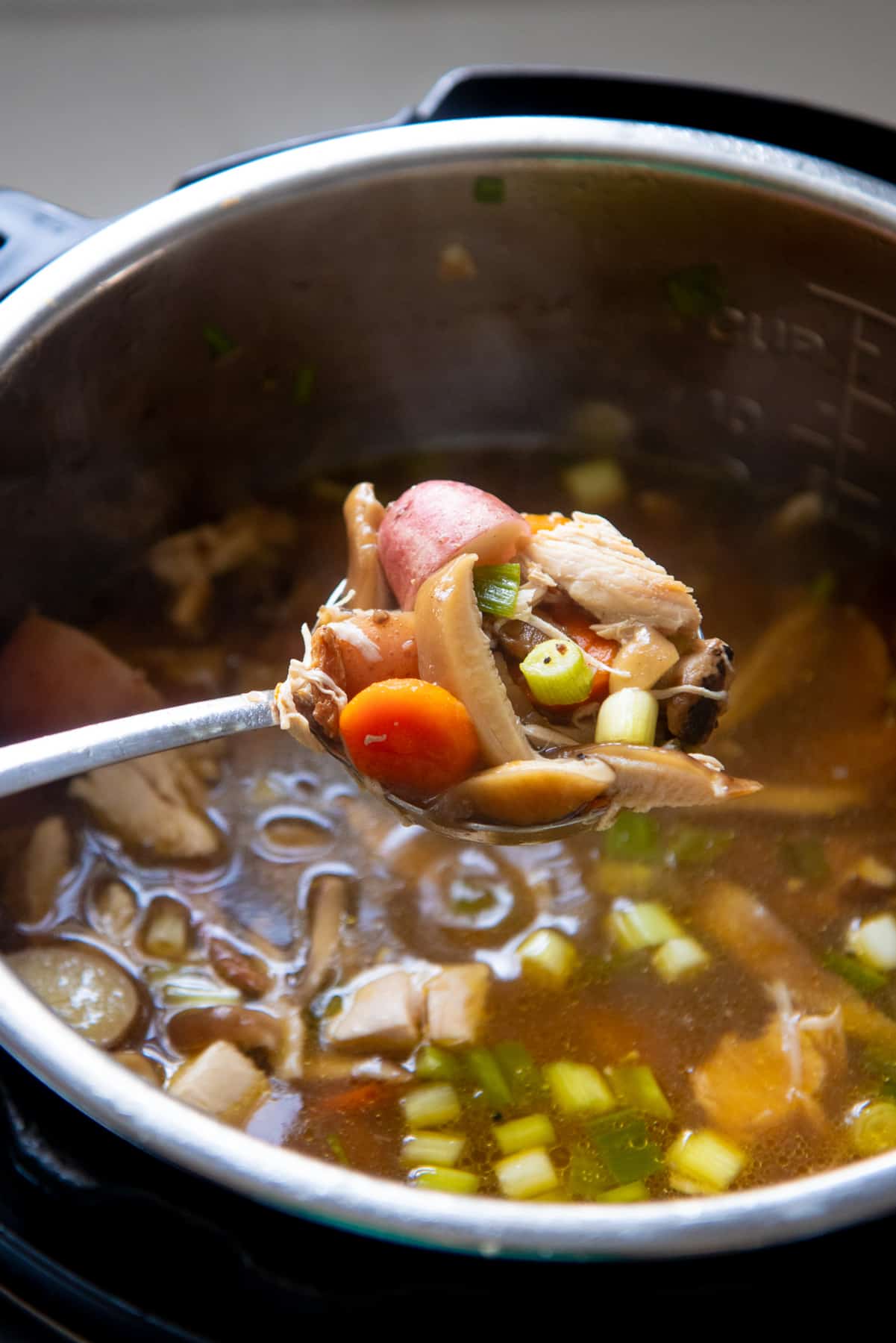 A spoon holds a scoop of soup over an open Instant Pot.