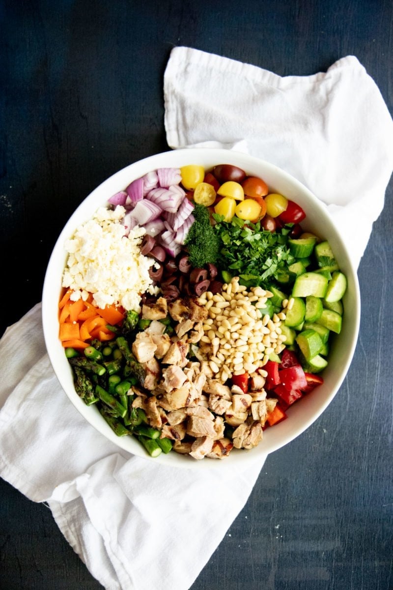 Overhead shot of ingredients for Grilled Chicken and Asparagus Chopped Greek Salad in a white bowl