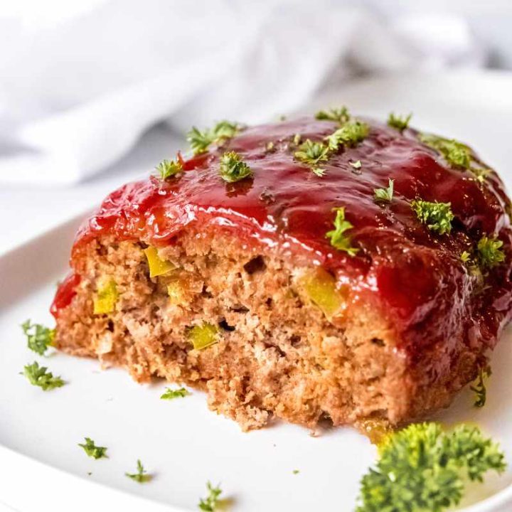 Classic meatloaf topped with a shiny glaze on a white plate with parsley garnish.