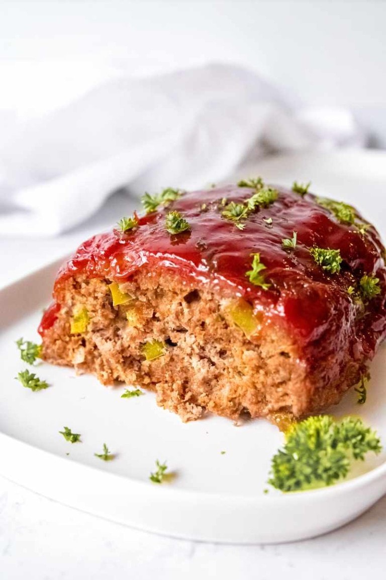 Classic meatloaf topped with a shiny glaze on a white plate with parsley garnish.