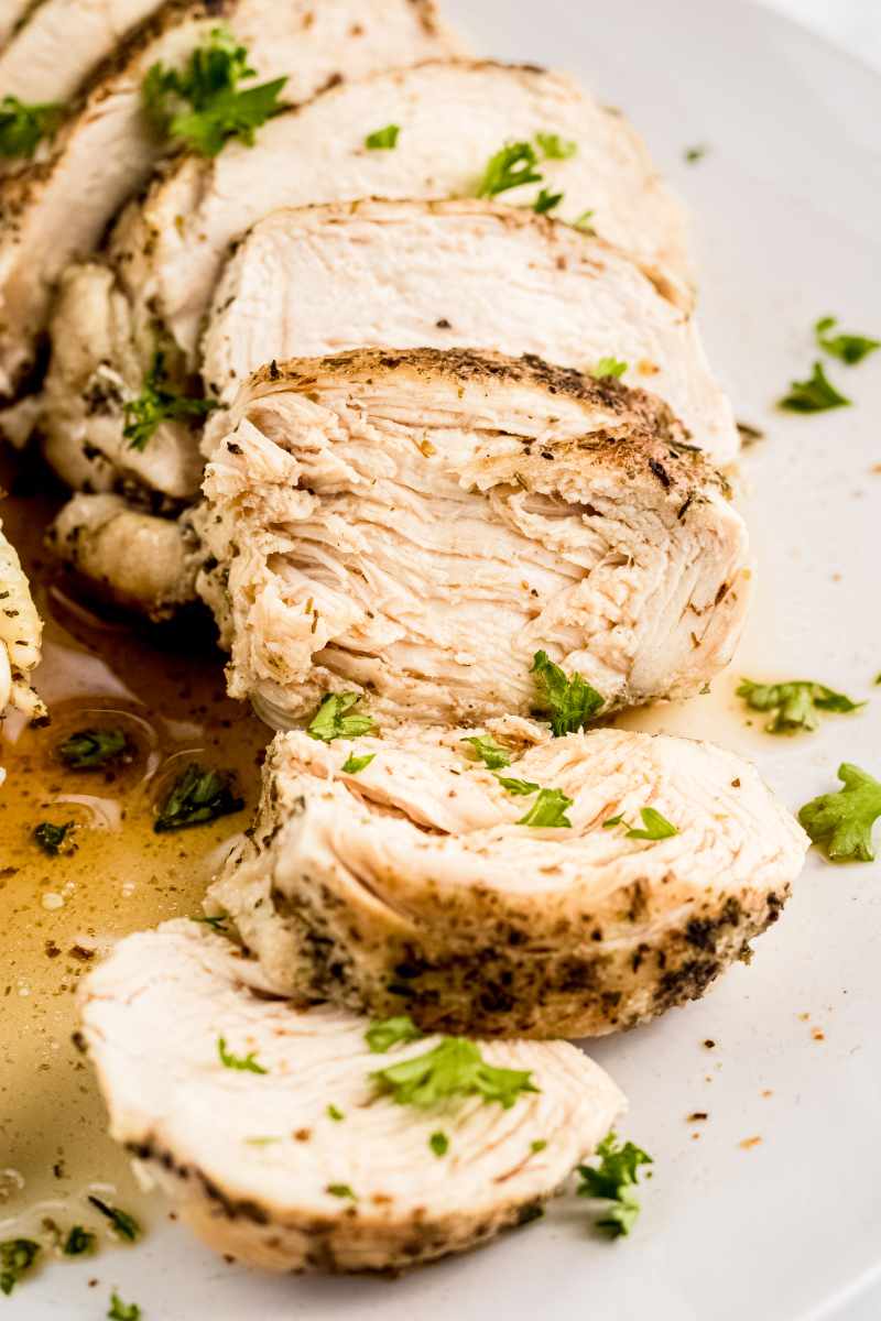 Close view of cooked chicken breast sliced on a white plate garnished with chopped fresh herbs.