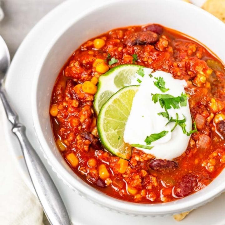 Close-up of full bowl of taco chili on a plate with spoon and tortilla chips.