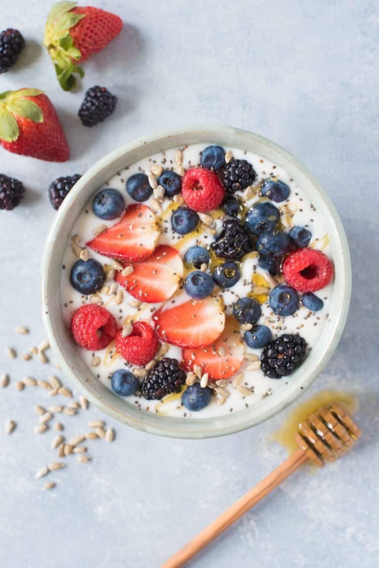 Overhead shot of Instant Pot coconut yogurt in a white bowl, garnished with mixed berries and seeds, and a drizzle of honey