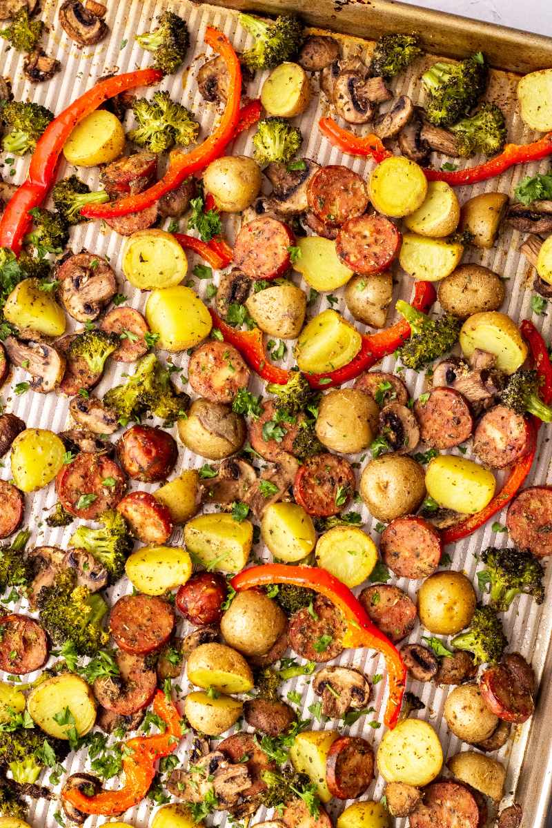 Overhead view of sheet pan sausage and veggies garnished with chopped fresh herbs.