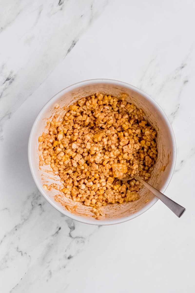 Corn kernels stirred together with dressing mixture in large white mixing bowl.