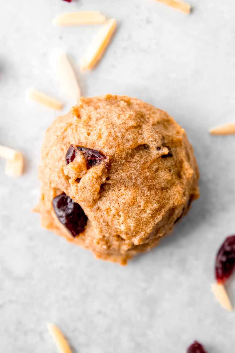 Top view of a cranberry almond breakfast cookie on a light counter with slivered almonds and dried cranberries around.