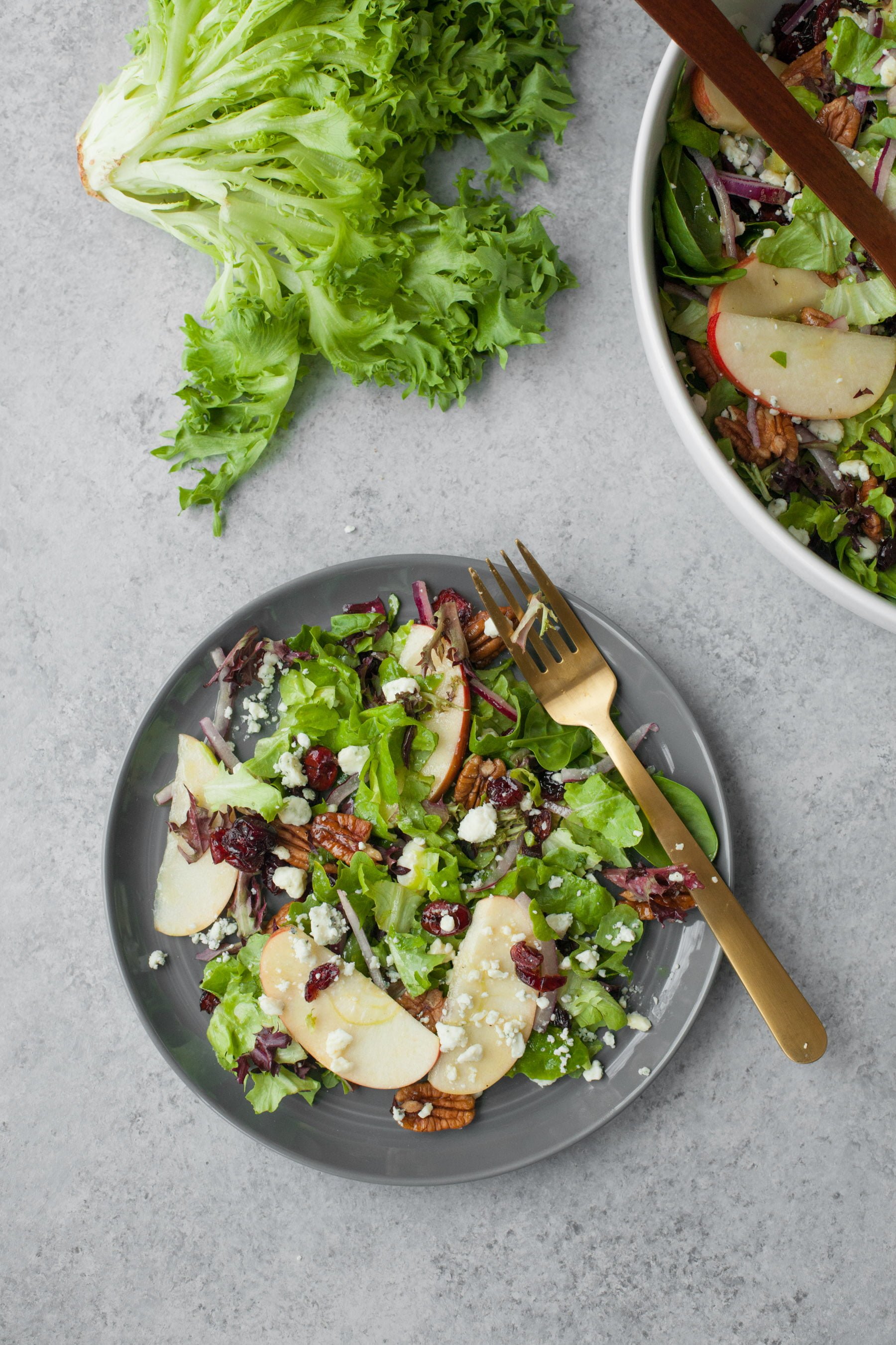 Top view of tossed and dressed salad on a plate alongside the full serving bowl.