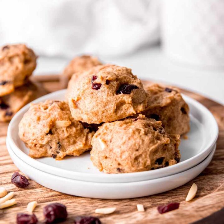 Soft cranberry almond cookies stacked on a white plate with additional cranberries and almonds around them.