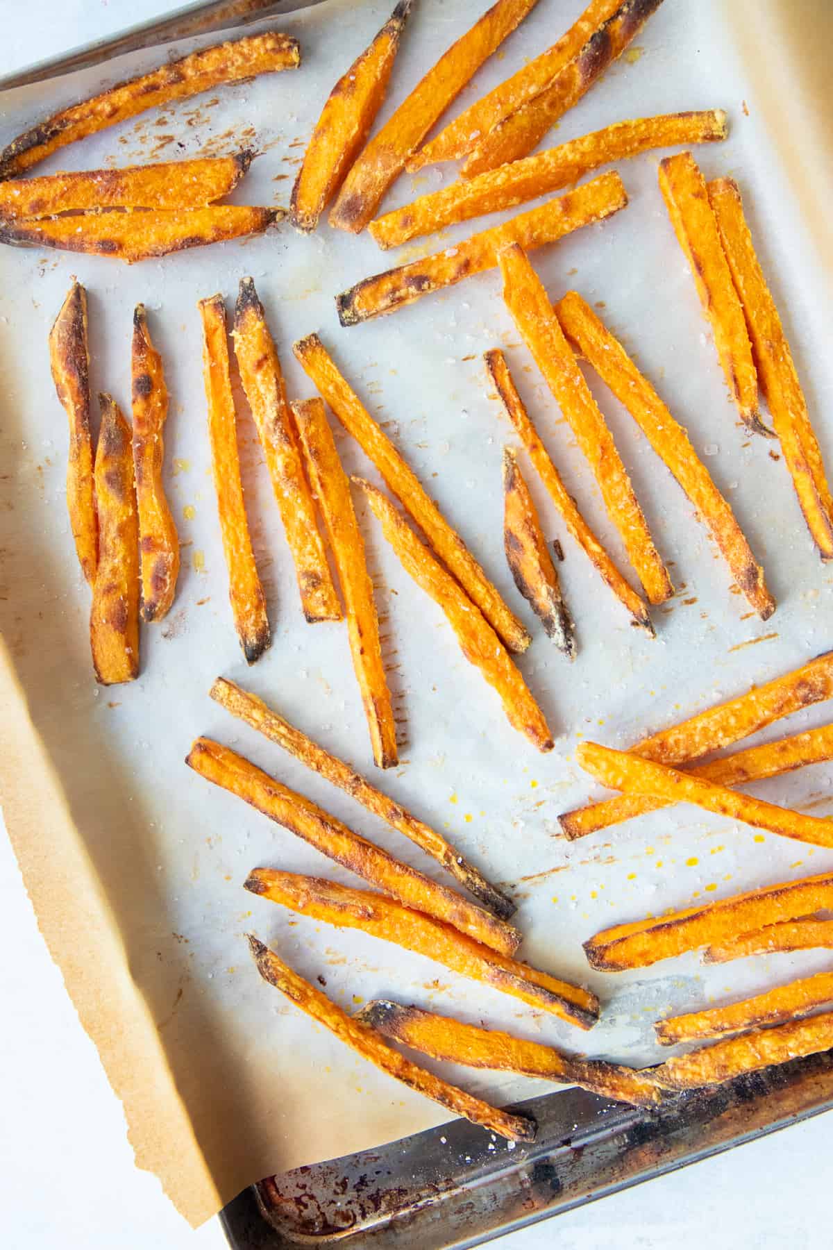 Baked fries spread out on a baking sheet lined with parchment paper.