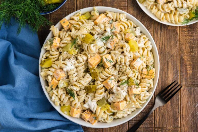 Top view of a bowl of dill pickle pasta salad on a wooden table with a blue kitchen linen and a fork.