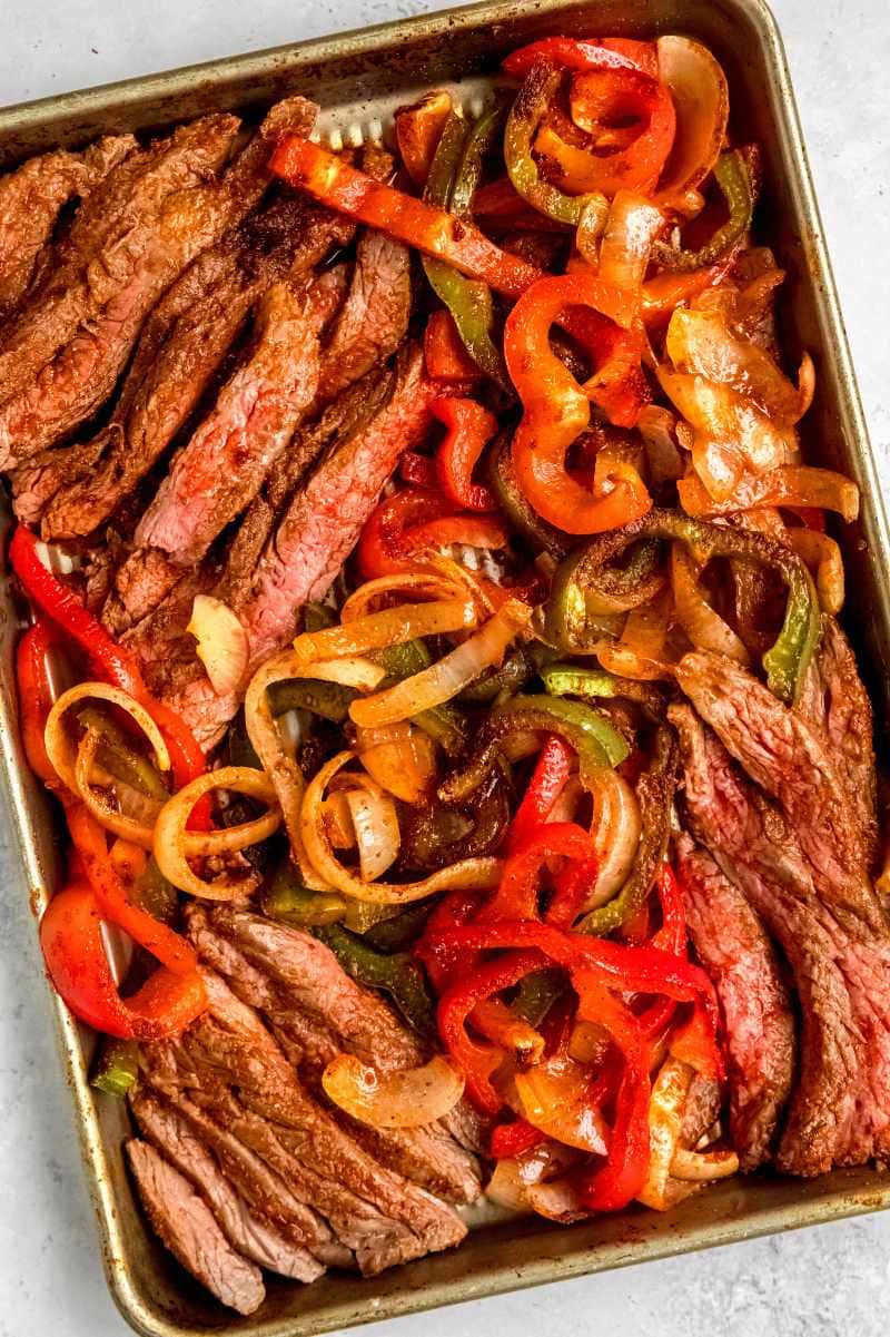 Overhead of a full fajitas dinner in a baking tray on a light counter.