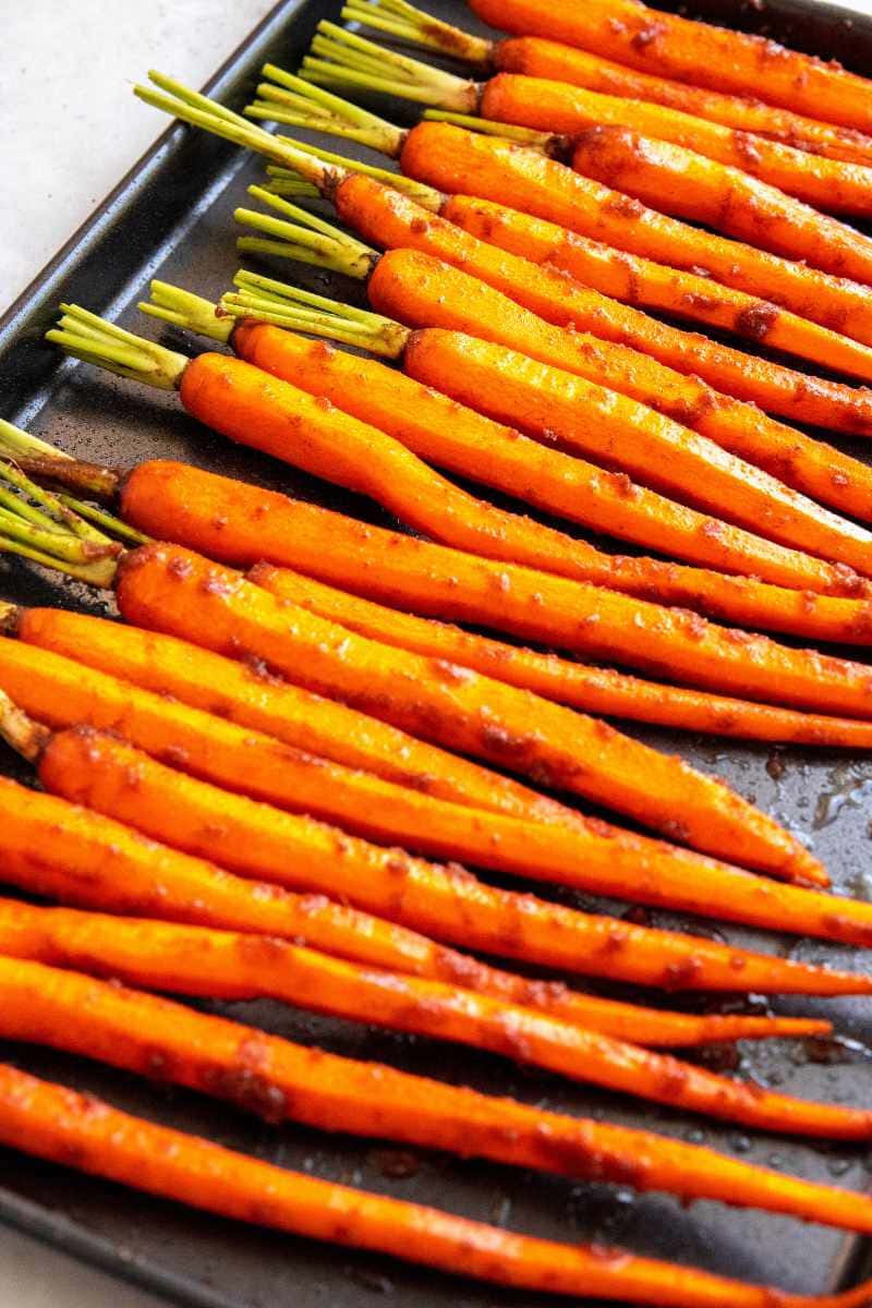 Trimmed and peeled carrots coated in a flavorful glaze lined up on a baking sheet in a single layer.