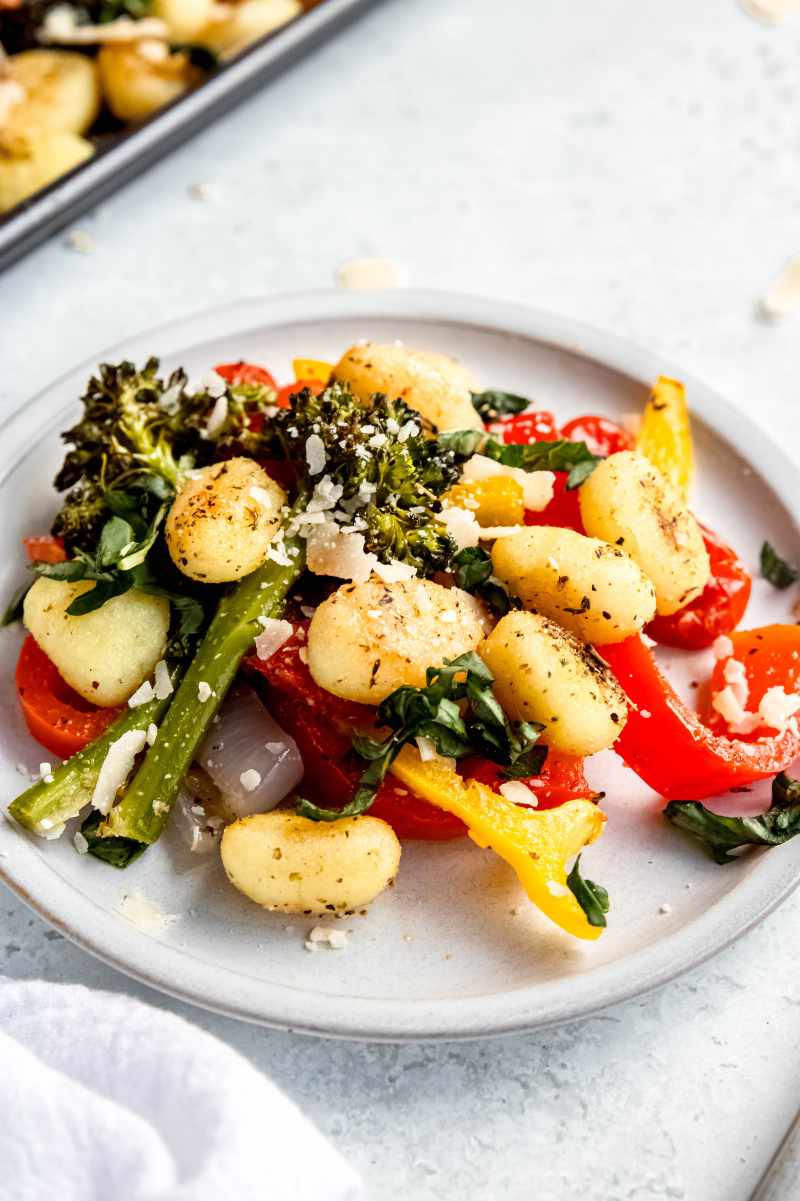 A single-serving platter of gnocchi and vegetables topped with parmesan cheese and fresh basil.