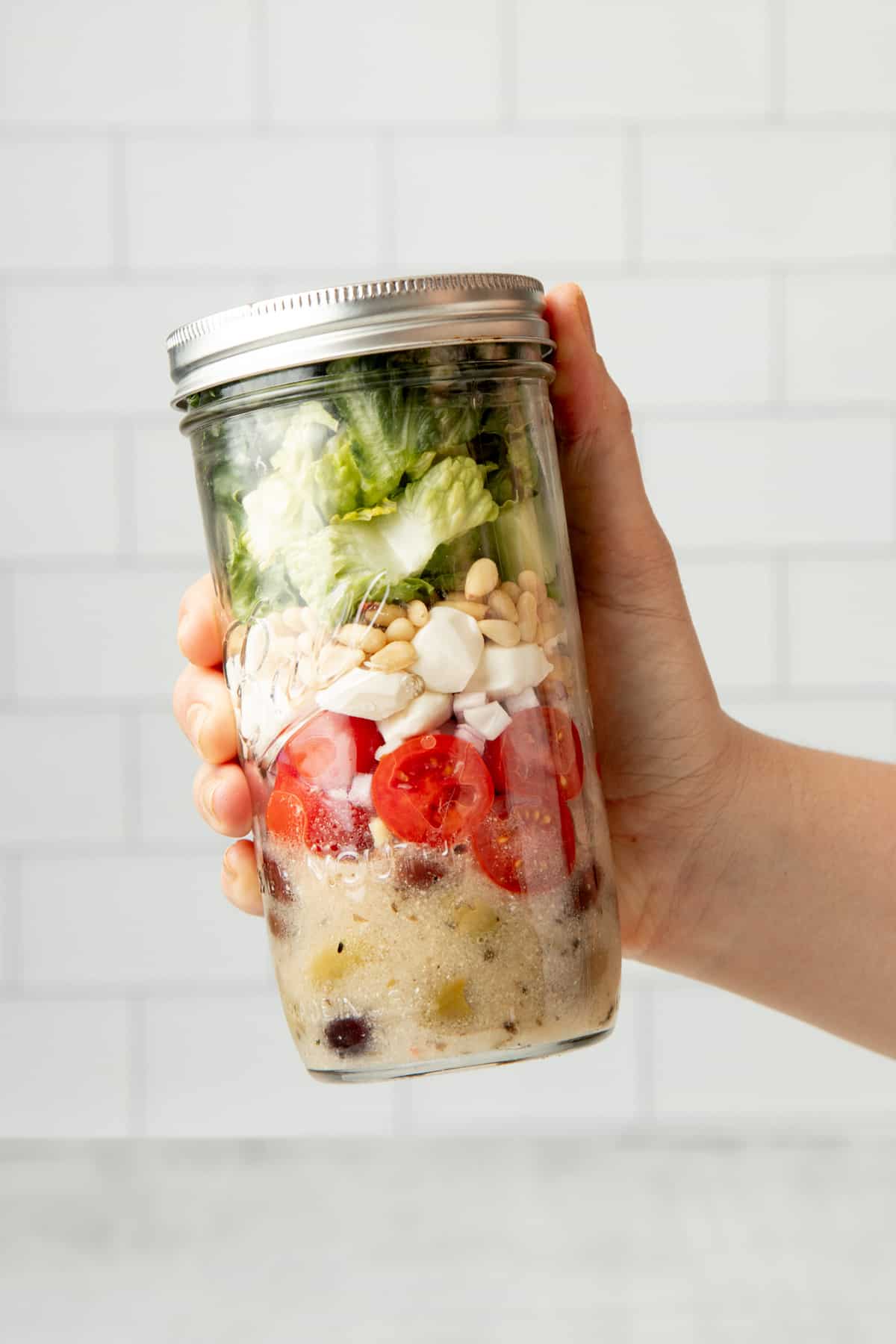 A hand holds a white-capped mason jar filled with an Italian chopped mason jar salad.