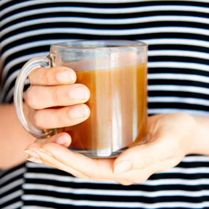 Clear mug of bone broth held in two hands