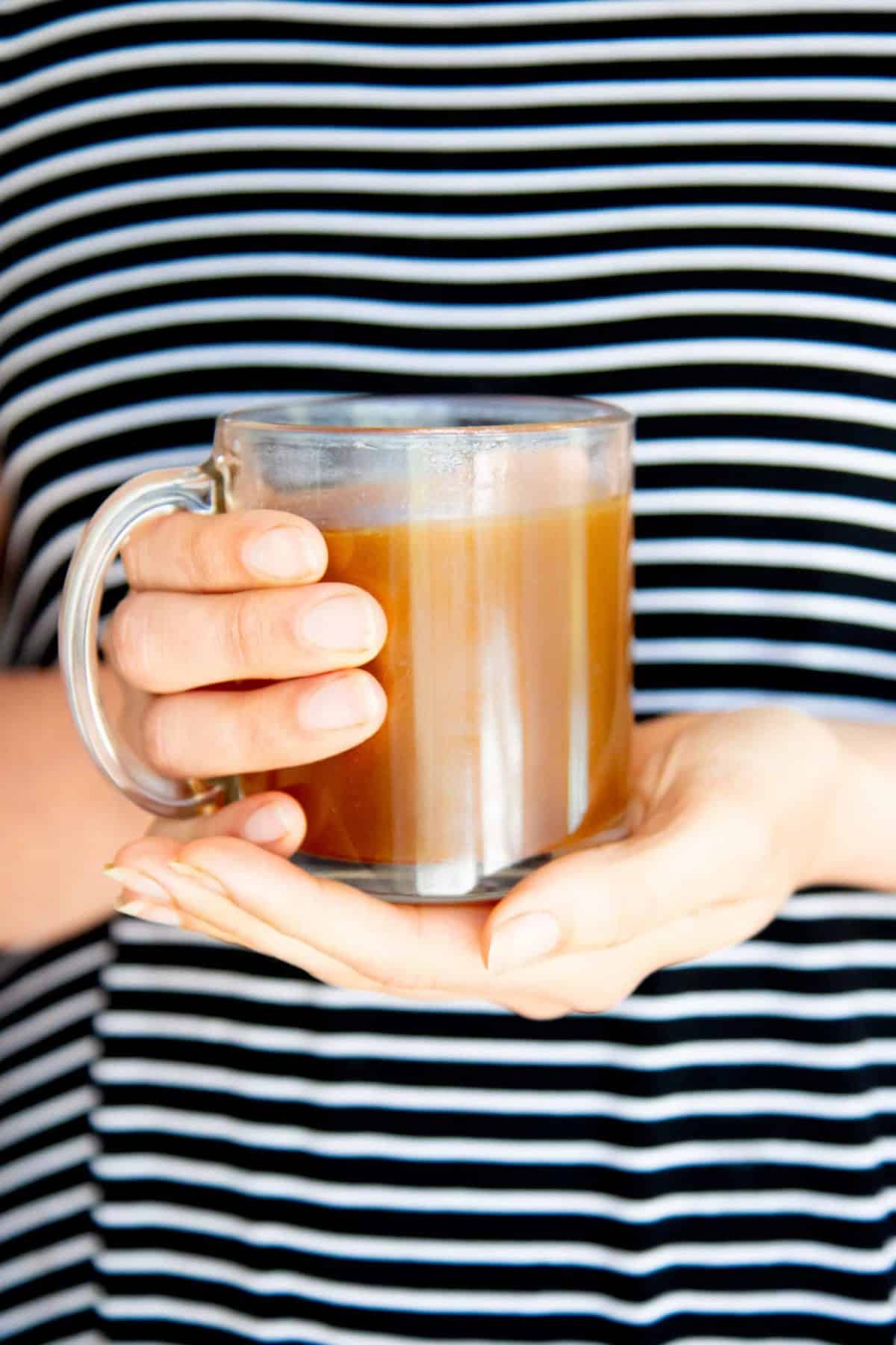 Clear mug of bone broth held in two hands