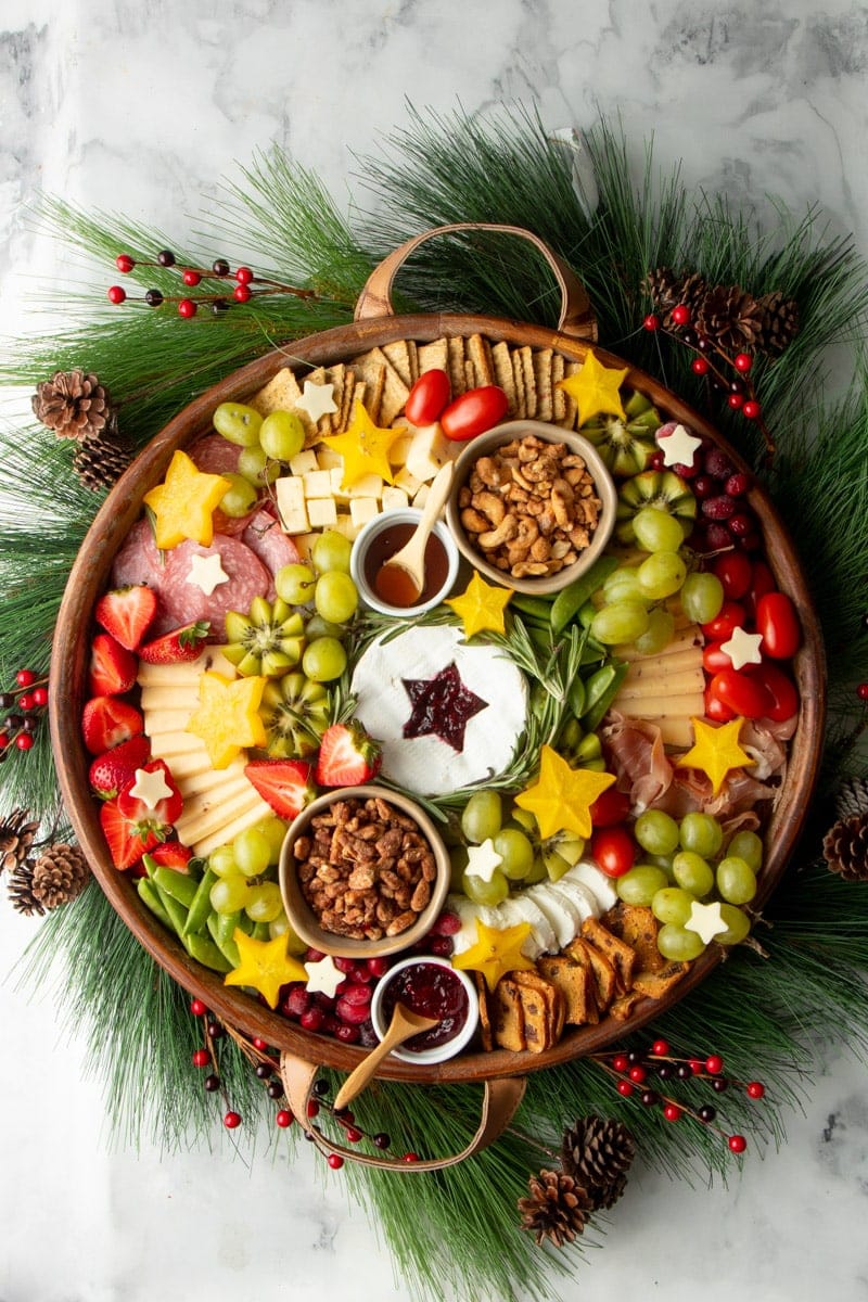 A holiday party appetizer served on a round platter filled with cheeses, meats, nuts, and fruits.