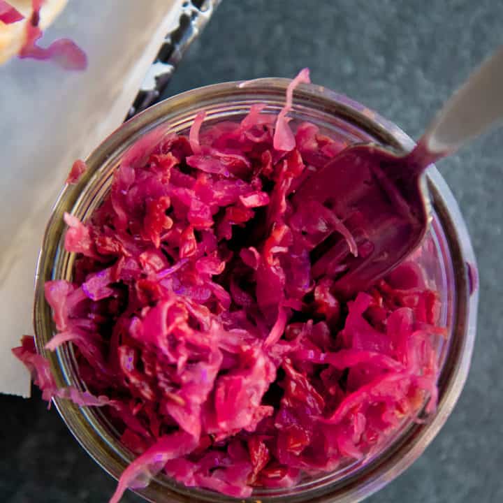 A fork dips into a glass jar of homemade sauerkraut.