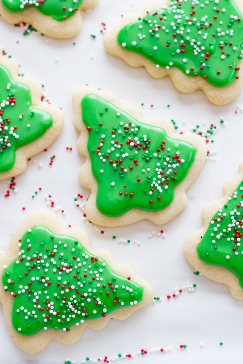 Decorated Christmas tree sugar cookies with green frosting and sprinkles rest on a white background.