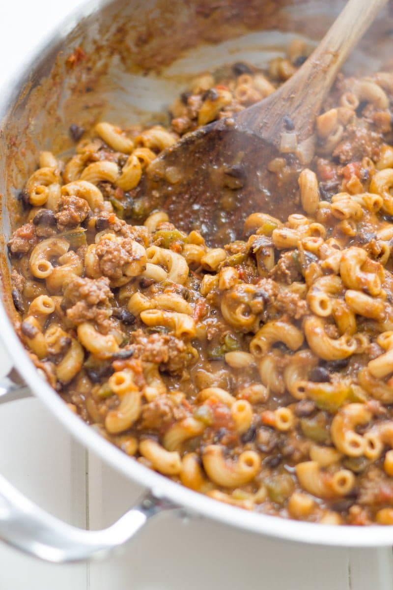 A pot of pasta and beef sits in a silver pan and is stirred by a wooden spoon.