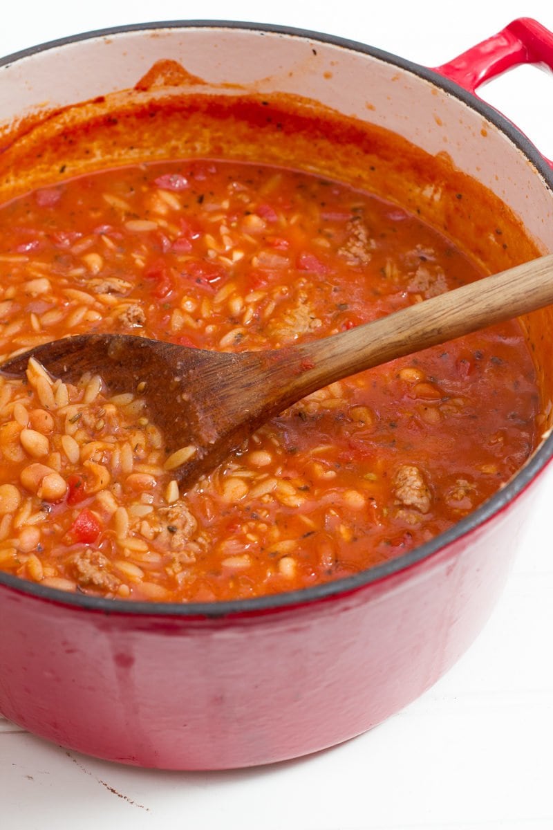 A dutch oven filled with soup ingredients is mixed together with a wooden spoon.