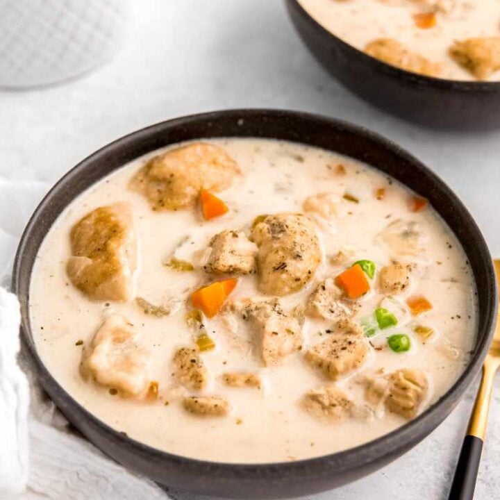 A dark serving bowl filled with creamy instant pot chicken and dumplings soup on a light background.