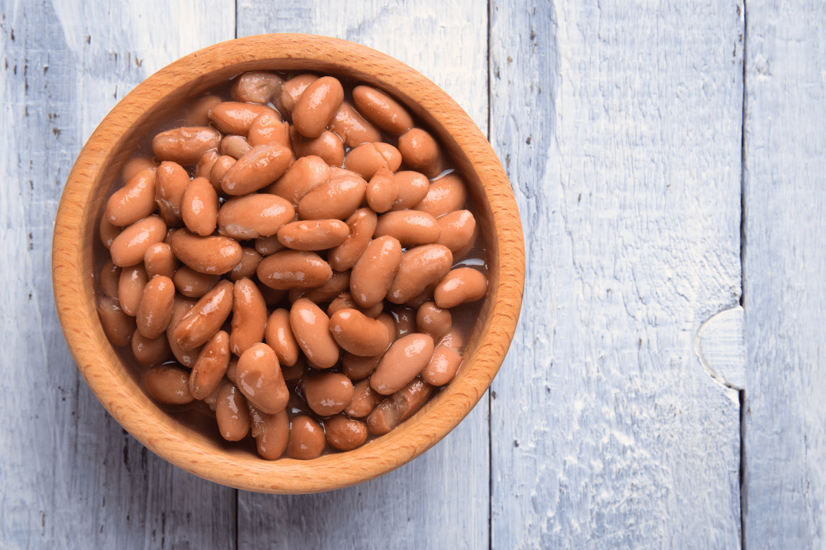 A wooden bowl of instant pot pinto beans rests on a light grey wooden table.