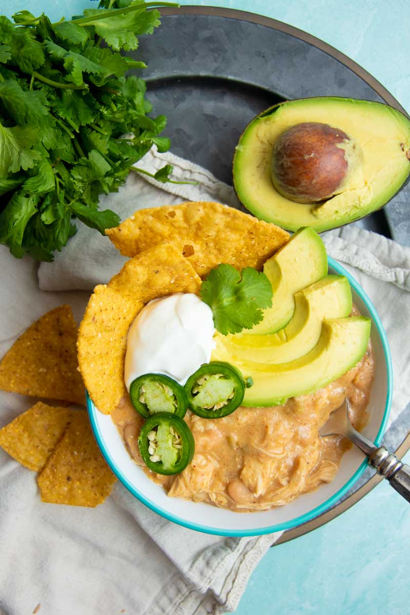 Top view of a bowl of white chicken chili on a serving tray with fresh cilantro, avocado, and jalapeno.